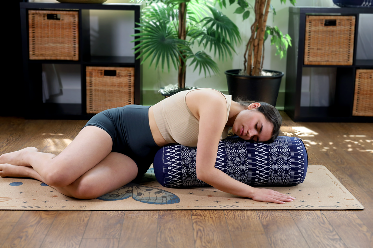 Woman lying on a yoga mat with a bolster in a home setting