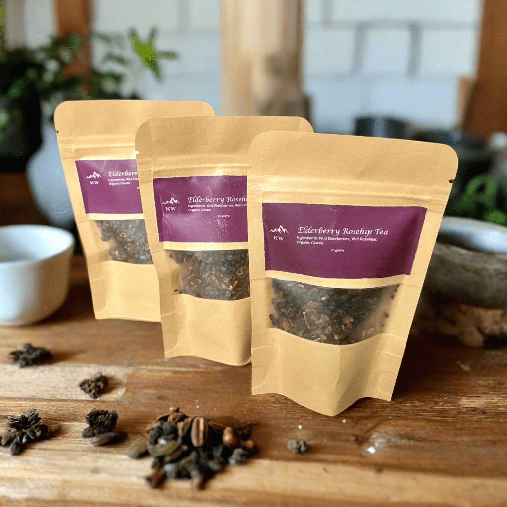 Three packages of Elderberry Rootship Tea on a wooden surface with loose tea leaves.