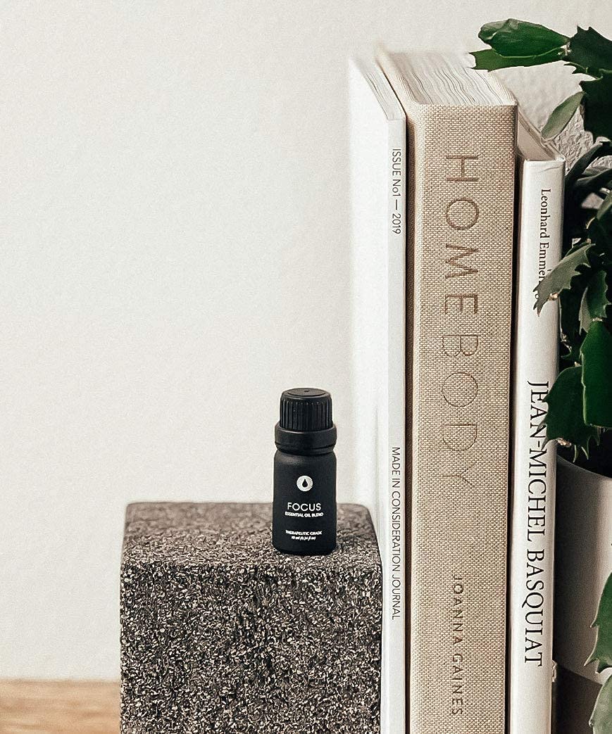 focus essential oil blend aromatherapy on a textured surface with books and a plant in the background.