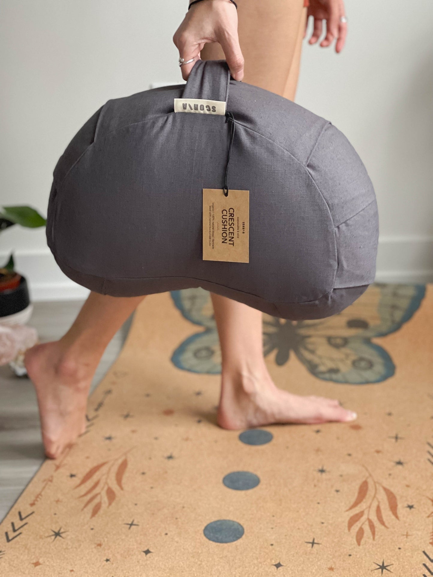 Person holding a gray yoga bolster on a patterned mat