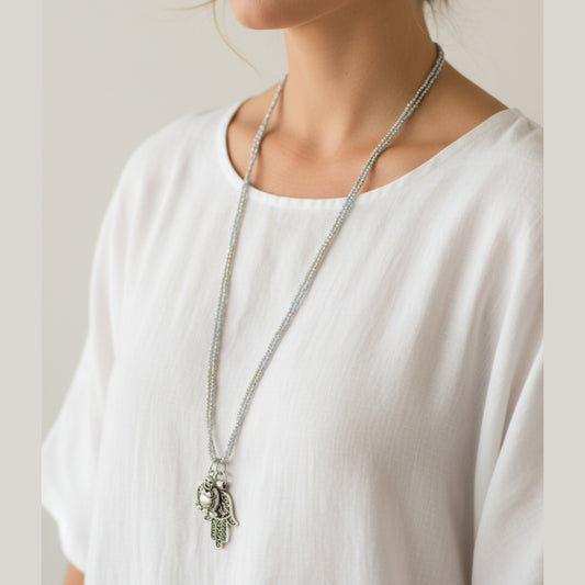 Long double-strand silver seed bead necklace with antique silver charm and ornate Hamsa hand pendant worn by a woman — handmade in India for boho, spiritual, and protective style