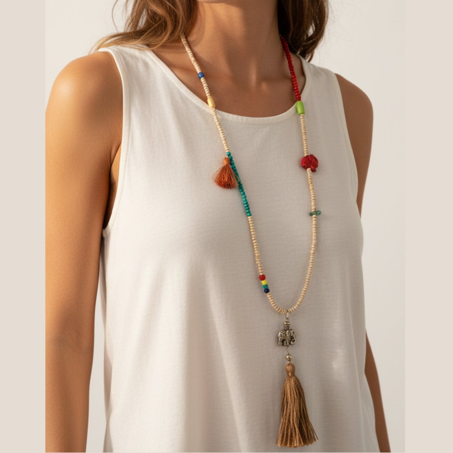 Long colorful mala necklace with cream seed beads, multicolor accents, mini tan tassel, red fabric elephant charm, antique silver elephant pendant and large tan tassel drop worn by a woman — handmade in India for boho and spiritual style