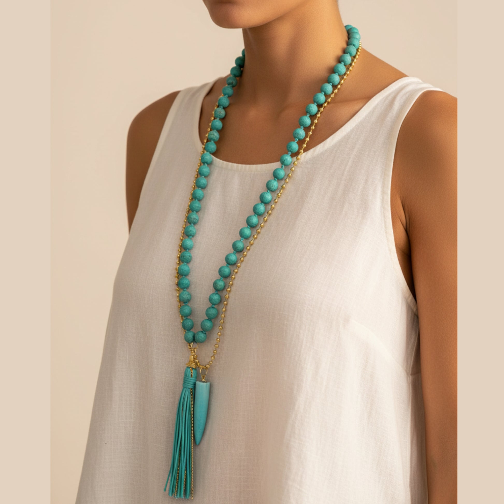 Long layered necklace with large turquoise round beads, gold ball chain, turquoise horn pendant and turquoise leather tassel worn by a woman — handmade in India for boho and statement style