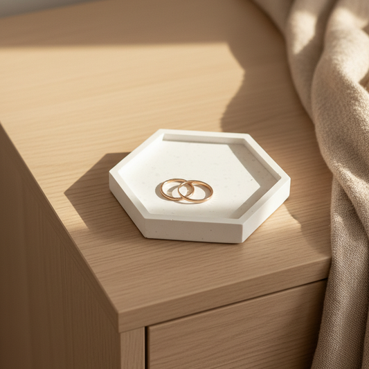 White speckled jesmonite hexagon trinket tray and jewelry dish with gold rings on a bedroom dresser in warm natural light
