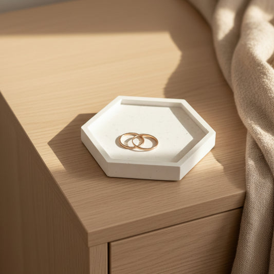 White speckled jesmonite hexagon trinket tray and jewelry dish with gold rings on a bedroom dresser in warm natural light