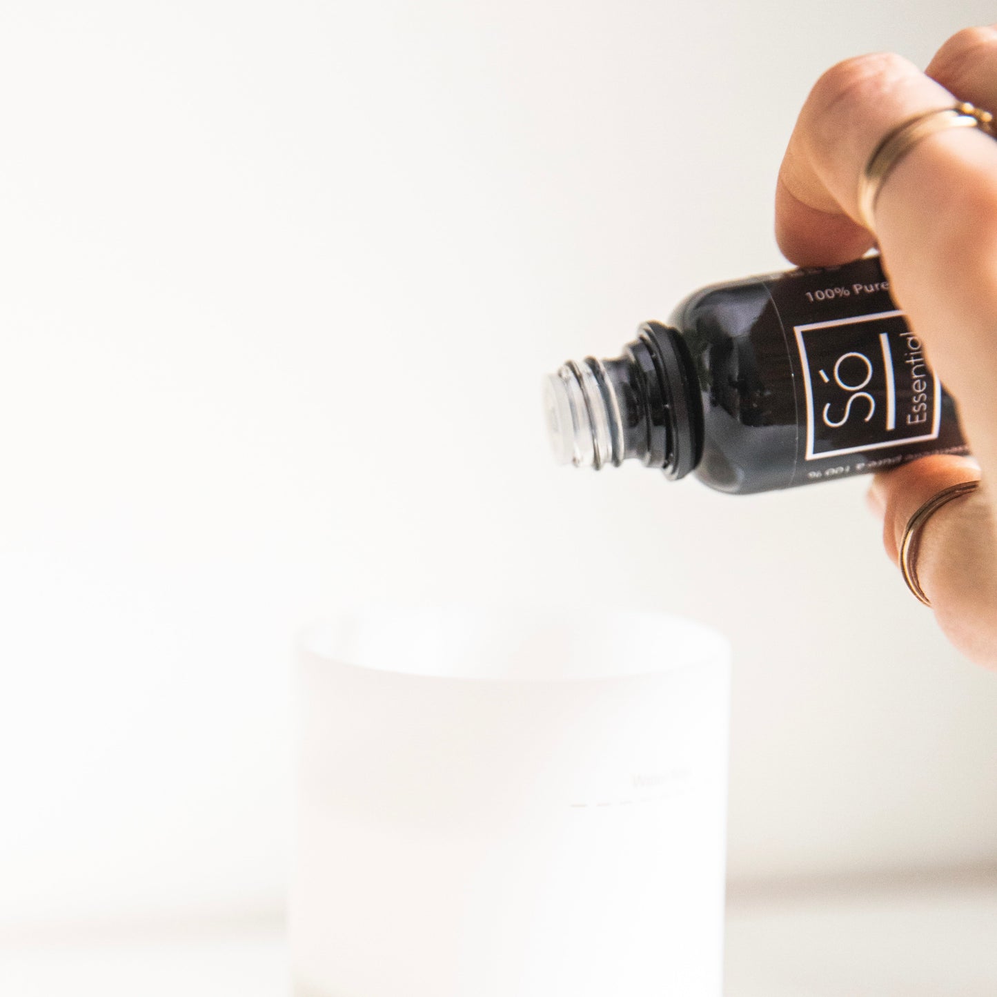 Hand holding a bottle of Só essential oil against a white background