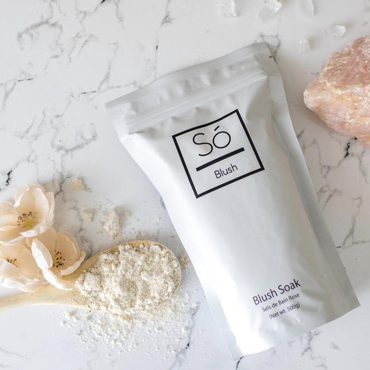 Blush Sóak - Bath Soak packaging on a marble surface with flowers and powder.