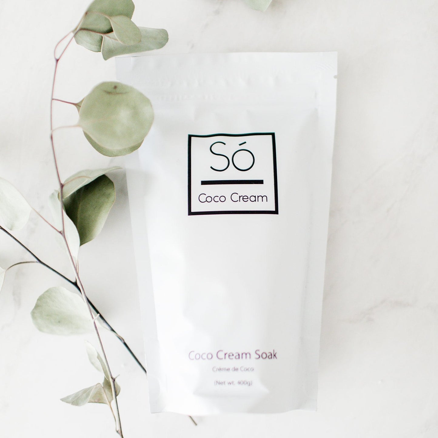 Coco Cream Soak packaging with a branch of eucalyptus leaves on a light background