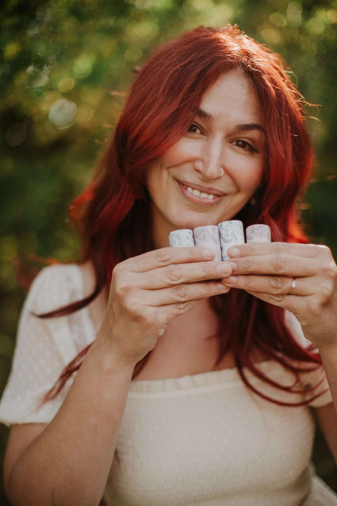 Woman holding four small lip balms against a blurred natural background