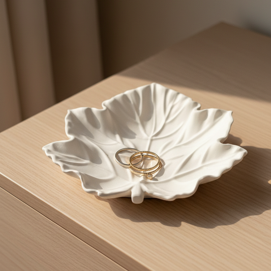Matte white maple leaf shaped jesmonite trinket tray and jewelry dish with gold rings on a dresser in an angled pose to see the leaf detail