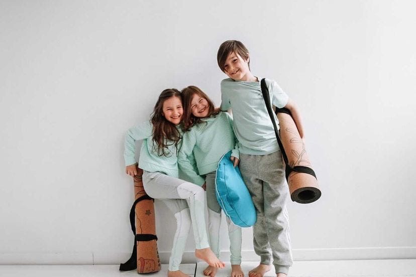 Three children in matching outfits with yoga mats on a white background