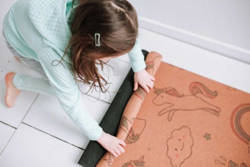 Child rolling out a kids size yoga mat with animal illustrations on a tiled floor