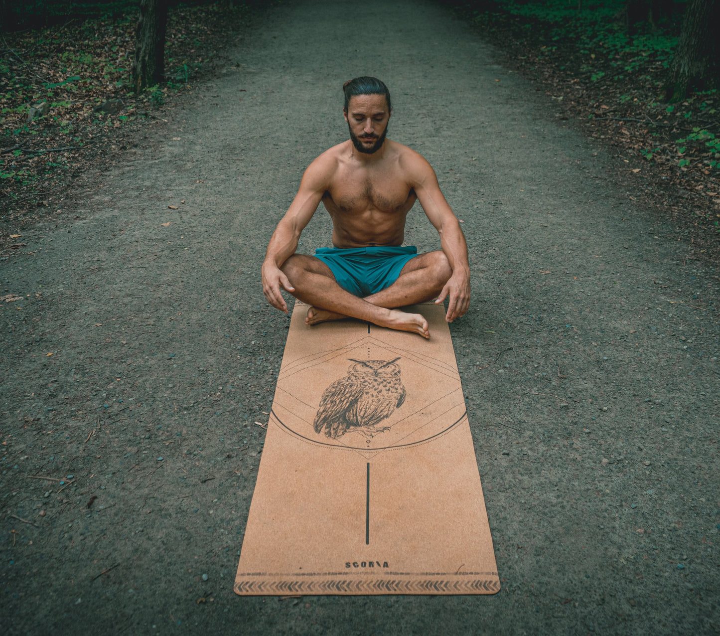 man sitting on a cork yoga mat with owl design outdoors