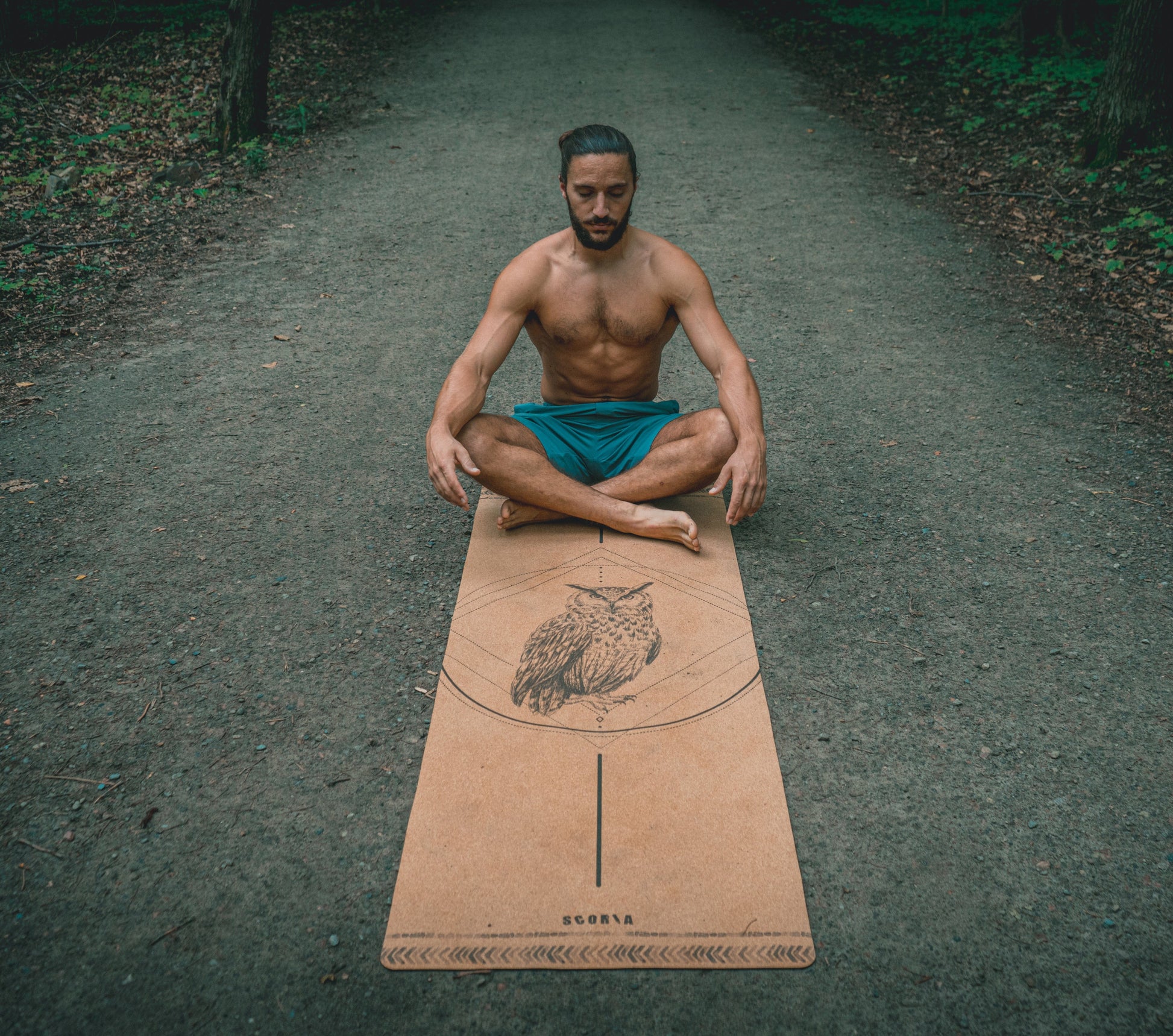man sitting on a cork yoga mat with owl design outdoors