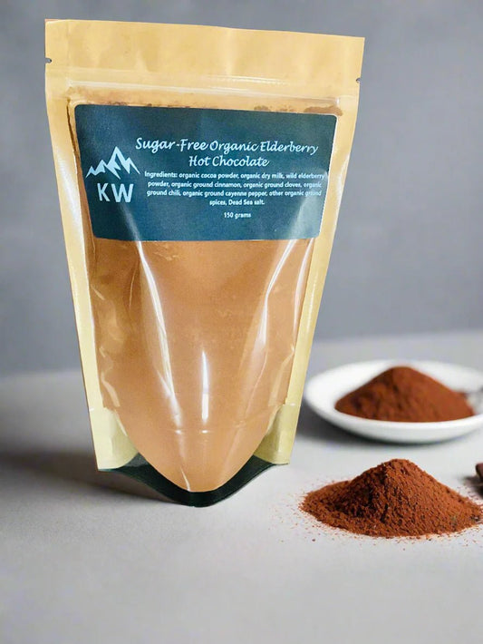Package of sugar-free organic elderberry hot chocolate with a small bowl and spoonful of powder on a gray background
