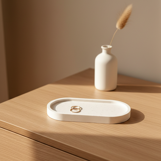 White speckled jesmonite oval trinket tray and jewelry dish with gold rings on a dresser in warm natural light