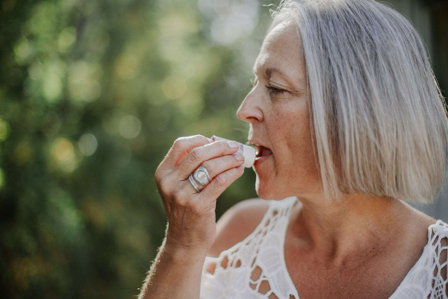 Woman applying lip balm outdoors with a blurred green background