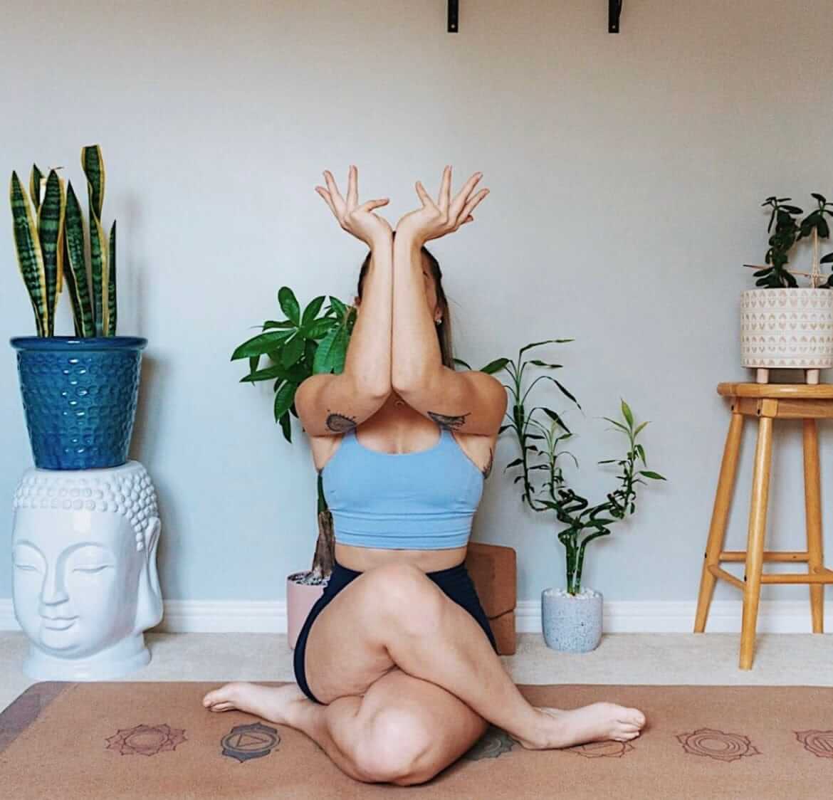 Person in a yoga pose on a cork yoga mat with chakra symbols with plants and a Buddha head in the background