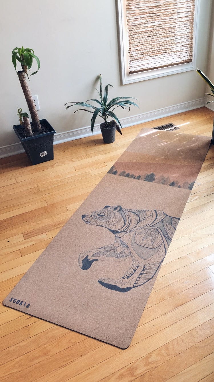 cork yoga mat with bear design on a wooden floor in a room with plants.