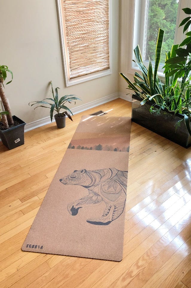 Yoga mat with bear design on a wooden floor in a room with plants and a window.