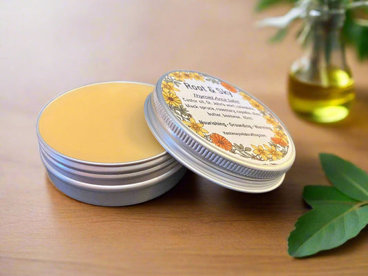 Throat and Neck Salve Balm in a tin with a decorative label on a wooden surface, surrounded by green leaves and a glass container.