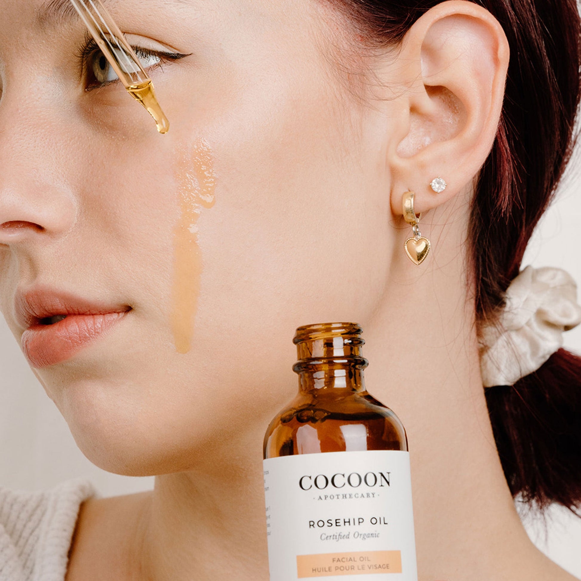 Woman applying Cocoon Rosehip Oil to her face with a dropper.