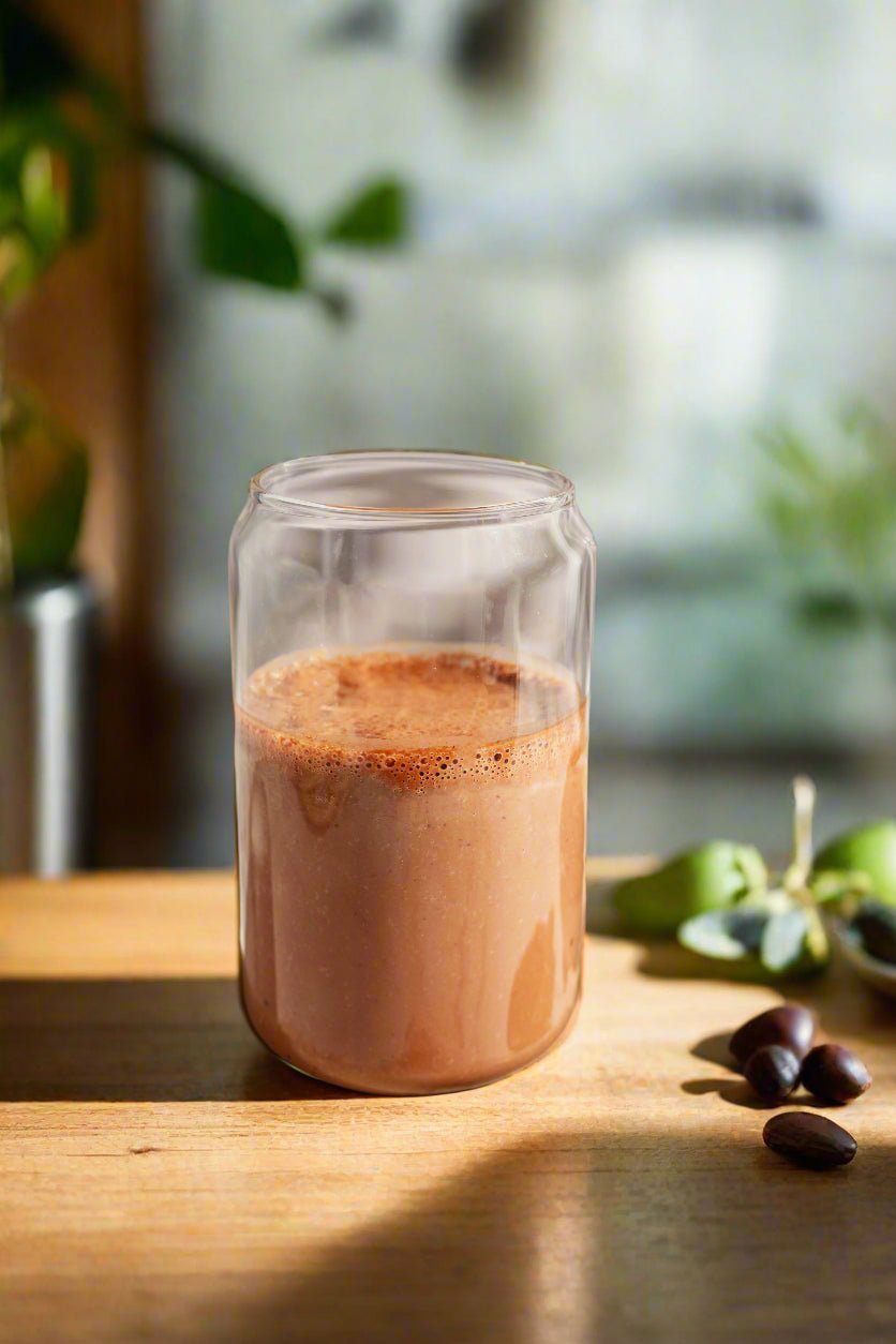 Glass of chocolate milk on a wooden surface with greenery in the background
