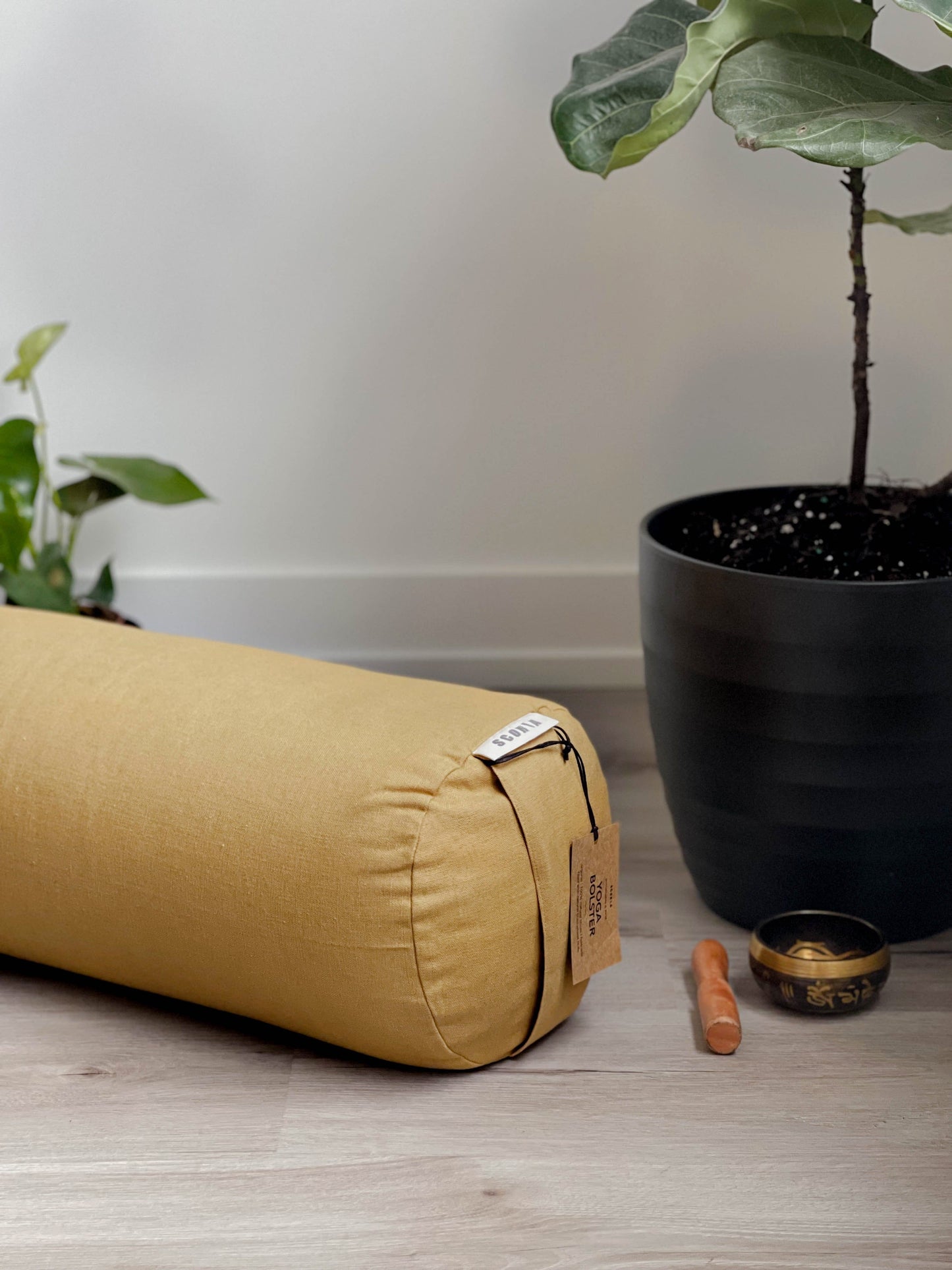 gold yoga bolster cylindrical pillow on a wooden floor with a plant and small bowl in the background.