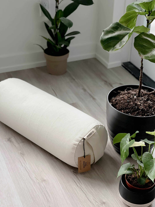 White cylindrical bolster pillow on a wooden floor with potted plants