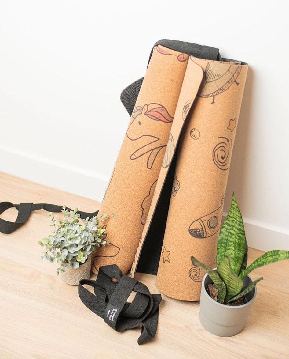 Two rolled-up kids' yoga mats with cartoon designs on a wooden surface with a plant and glasses.
