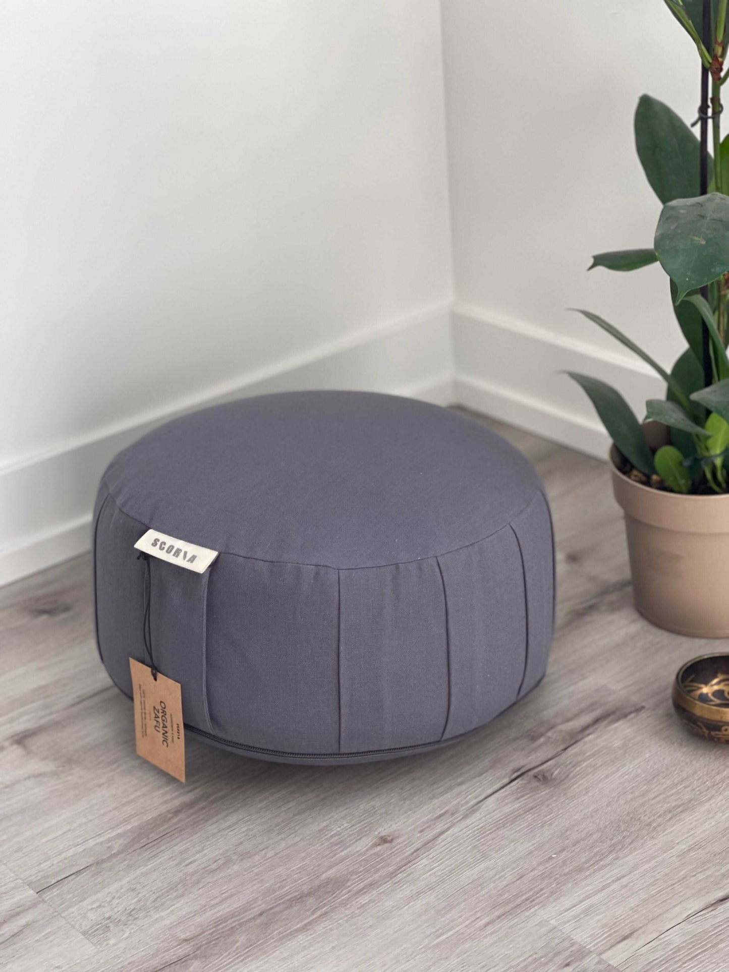 Gray fabric yoga pillow with a tag on a wooden floor next to a plant
