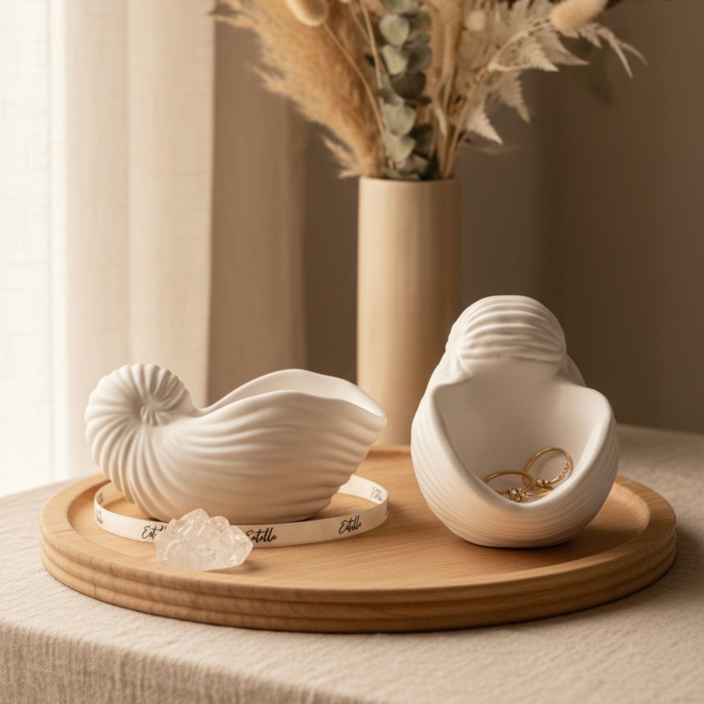 Matte white nautilus and spiral sea shell shaped jesmonite trinket trays styled on a dresser with gold jewelry, crystals, and dried botanicals in warm natural light