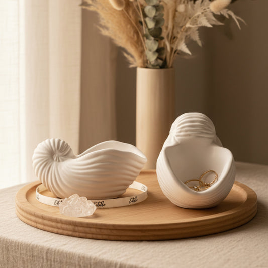 Matte white nautilus and spiral sea shell shaped jesmonite trinket trays styled on a dresser with gold jewelry, crystals, and dried botanicals in warm natural light