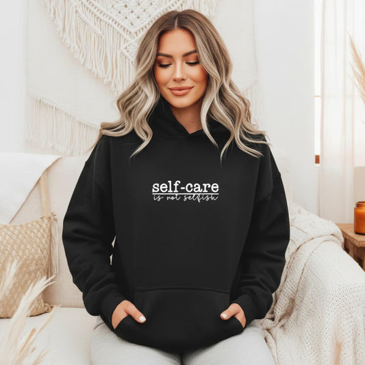 Women's pullover hoodie in black with "Self Care Is Not Selfish" print — mental health gift for women who are learning to put themselves first