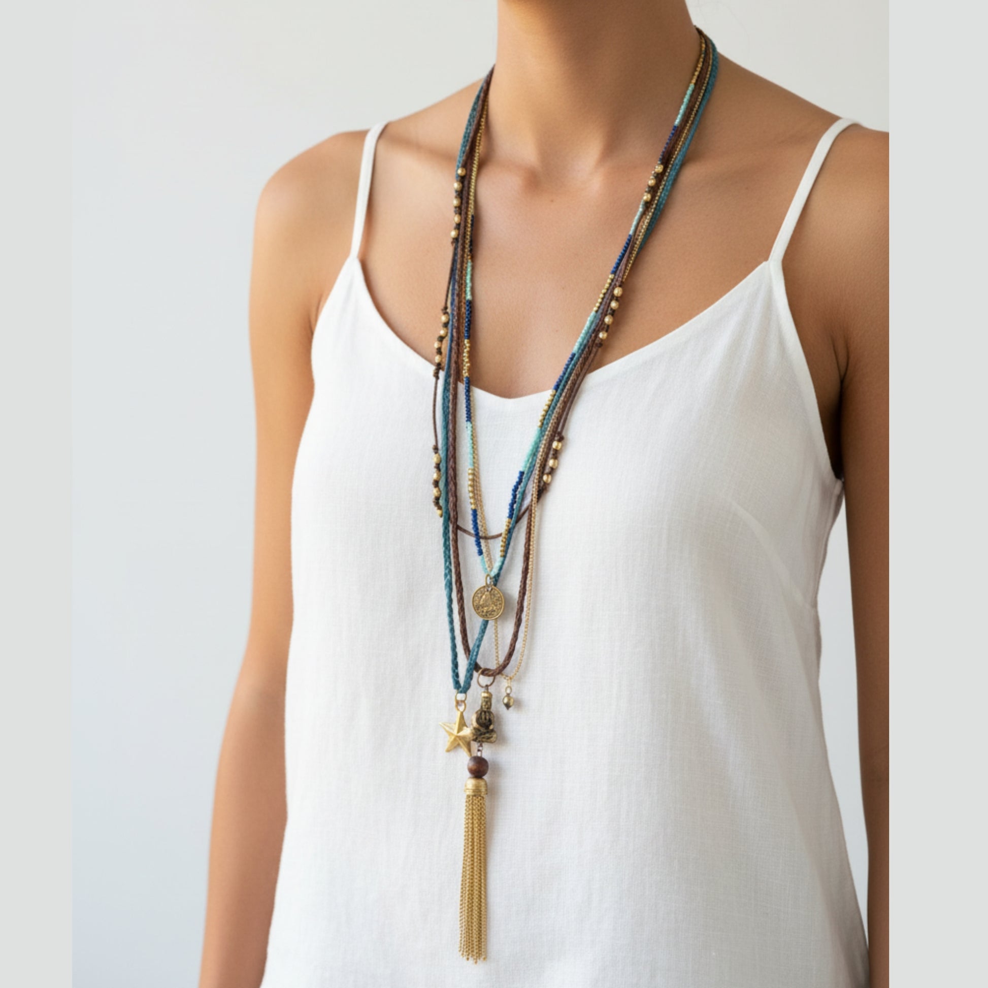 Layered multi-strand boho necklace with blue seed beads, gold chains, coin pendant, star charm, sitting Buddha charm and long gold chain tassel worn by a woman — handmade in India for spiritual and statement style