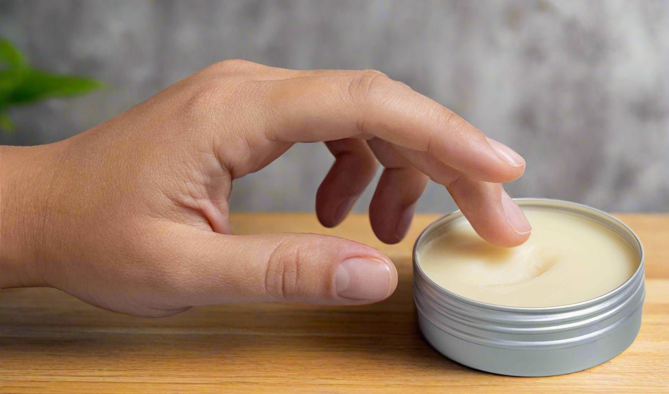 Hand applying Pure Tallow Balm from a small container on a wooden surface with a neutral background