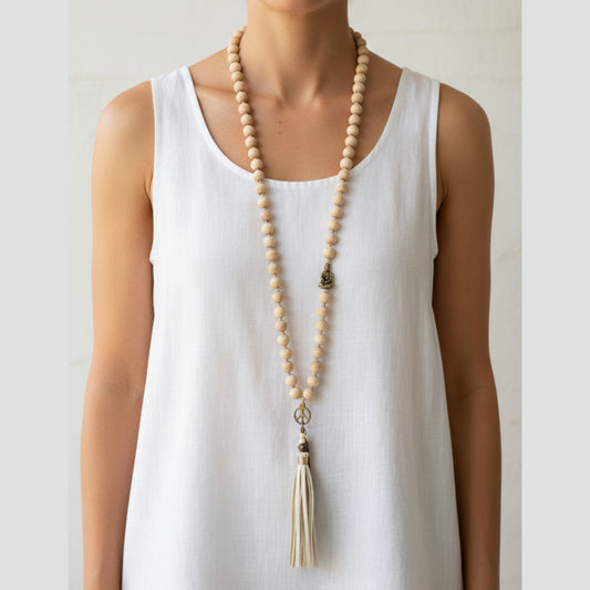 Long natural wood bead mala necklace with antique gold Buddha charm, peace sign pendant and cream leather tassel worn by a woman — handmade in India for boho, yoga, and spiritual style