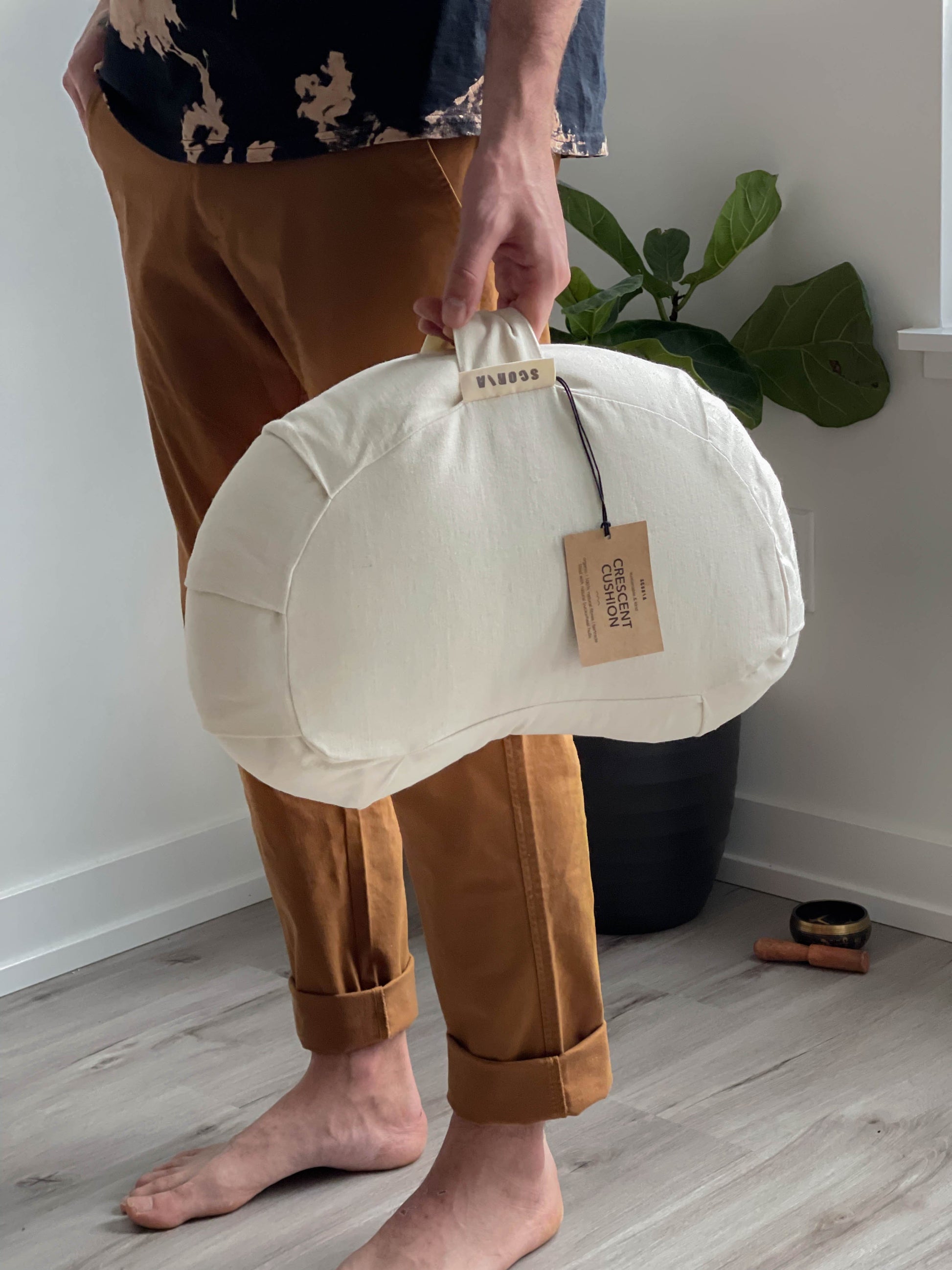 Person holding a white yoga cushion  with a visible brand tag indoors.