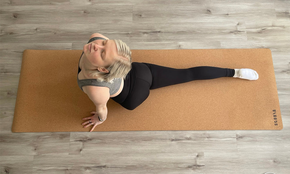 Person practicing yoga on extra tall cork yoga mat with a wooden floor background